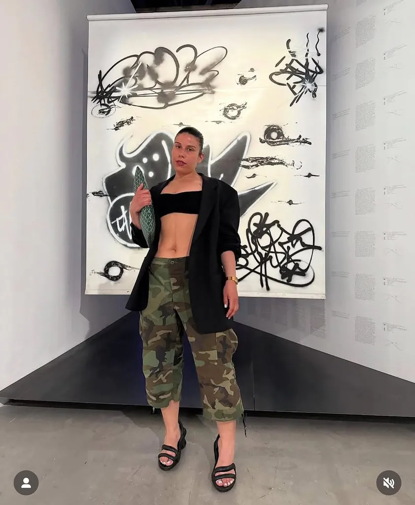 woman wearing a black blazer and camouflage cargo shorts in front of artwork