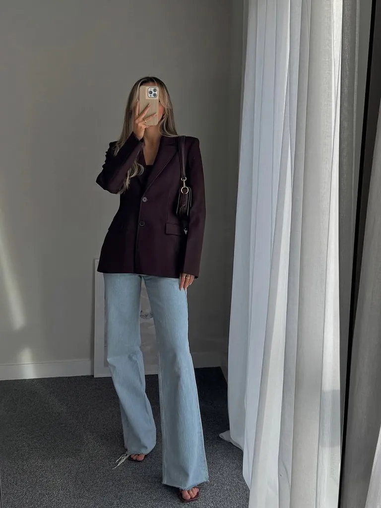 woman taking mirror selfie wearing a dark brown blazer and light blue jeans
