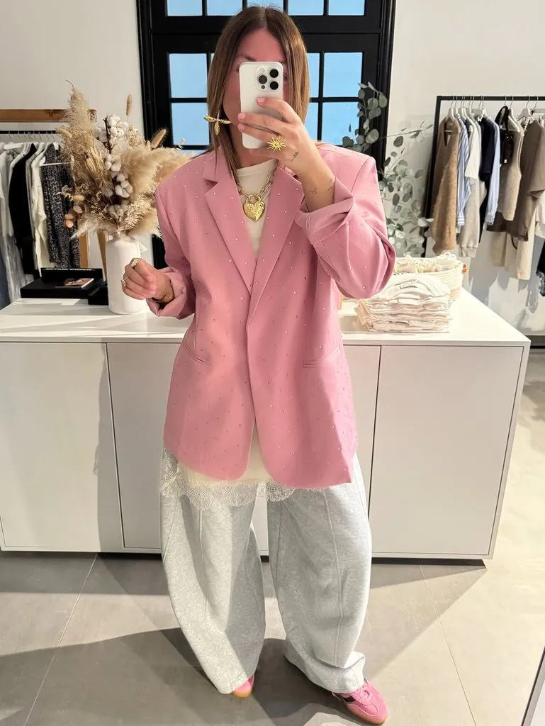 person taking mirror selfie wearing a pink embellished blazer and grey sweatpants