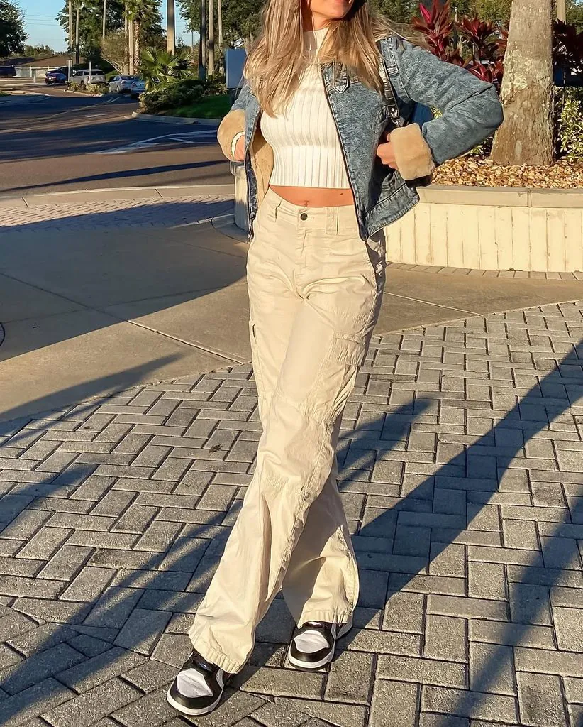 woman wearing cropped white top, denim jacket, and beige cargo pants outdoors
