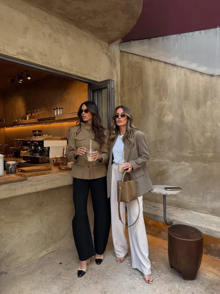 two stylish women holding iced drinks standing in front of a modern coffee shop