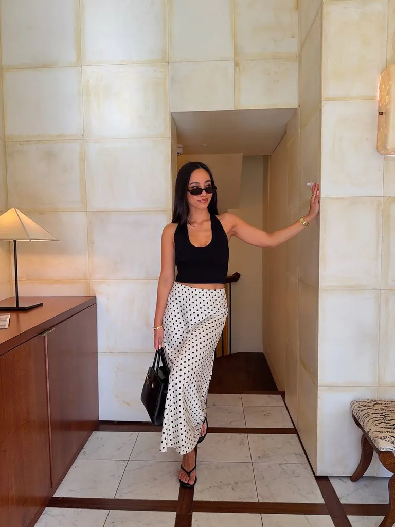 woman in black halter top and polka dot maxi skirt standing indoors