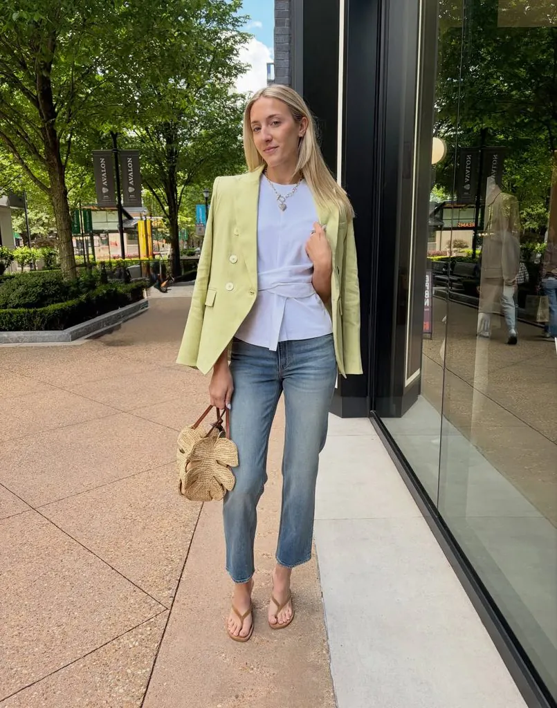 woman wearing light green blazer, white top, and blue jeans outdoors