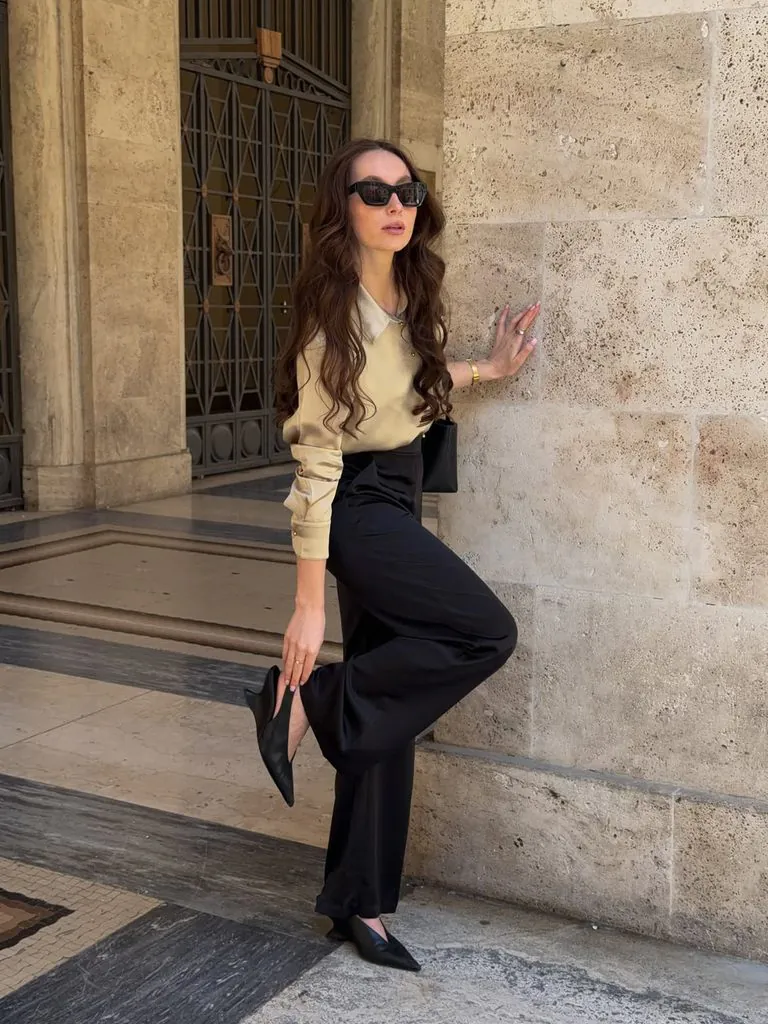 woman wearing a beige satin blouse black wide-leg trousers and pointed heels outdoors